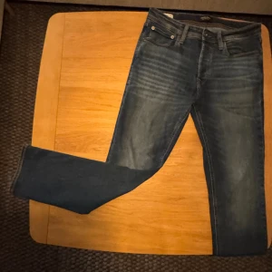 Blå straight jeans från Jack & Jones - Snygga blå jeans från Jack & Jones i modellen Slim Straight/Tim. Klassisk femficksdesign med raka ben och normal passform. Jeansen har subtila slitningar framtill och är tillverkade i slitstarkt denimtyg. Perfekta för dig som gillar enkel och stilren look. Storlek 29/30