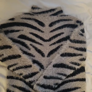 Zebramönstrad fluffig tröja NA-KD XS - Supermjuk och fluffig zebramönstrad tröja från NA-KD i svart och grått. Tröjan har hög hals och långa ärmar, perfekt för dig som vill sticka ut med en cool look. Materialet är stickat och känns riktigt cozy.