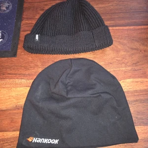 Svarta mössor, stickad & Hankook - Två svarta mössor säljes! En ribbstickad variant med uppvikt kant och liten etikett, perfekt för chill stil. Den andra är en slät bomullsmössa med Hankook-logga broderad i vitt och orange. Båda är enkla och passar till allt.