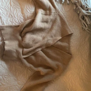 Beige omlottstickad kofta - Mysig beige stickad kofta med omlottmodell och breda muddar. Tröjan har ribbad struktur och långa ärmar, perfekt för lager-på-lager under kyliga dagar. Enkel att styla till både jeans och kjol.