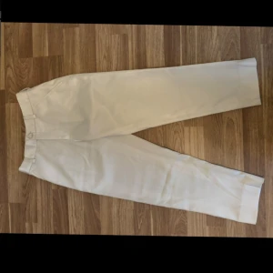 Vita kostymbyxor med rak passform - Snygga vita kostymbyxor med klassisk rak siluett och pressveck. Byxorna har hällor för bälte och diskreta sidofickor. Perfekta för en clean och stilren look, tillverkade i ett mjukt material som ger en skön känsla.