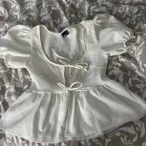 Vit blus med puffärm från Gina Tricot - Superfin vit blus från Gina Tricot med puffiga korta ärmar och två söta knyt framtill. Blusen har en lätt rynkad struktur och en volang nedtill. Står xs men passar mig som är ofta S 