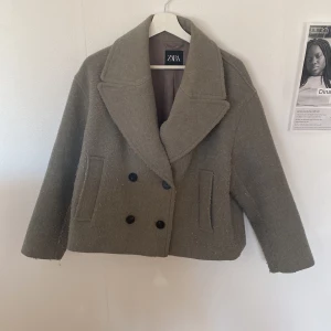 Beige skepparkavaj från Zara, M - Säljer en beige skepparkavaj från Zara i storlek M. Jackan har bred krage, dubbelknäppning med svarta knappar och två fickor fram. Materialet är ullblandning och modellen är croppad med loose passform. Perfekt för dig som gillar stilrena och trendiga plagg.