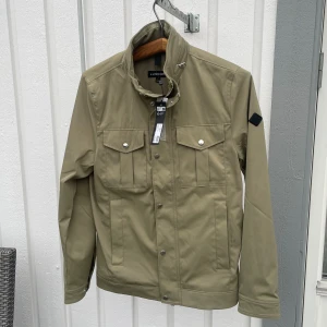 Grön J.lindeberg Bailey Poly Jacket (Helt ny) - S - Jag säljer den här riktigt snygga J.lindeberg jackan som är helt ny med tagen kvar. Den är i den populära modellen Bailey Poly och är i storlek S men passar även M. Nypris ligger på 3400kr och jag säljer den här för 1699kr. Tveka inte att höra av er!