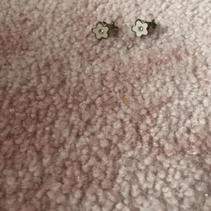 Söta vita blomclipsörhängen  - Ett par små och gulliga clipsörhängen formade som blommor i vit färg med en liten glittrande detalj i mitten. Metallfärgad kant runt blomman ger en stilren touch. Perfekt för dig som gillar blommiga accessoarer och vill ha något enkelt men inte har hål i öronen.