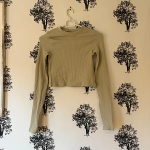 Grön ribbad långärmad topp - Säljer en beige croppad topp med lång ärm och ribbad struktur. Toppen har en rund halsringning och är figurnära i modellen. Perfekt att styla med höga jeans eller kjol för en clean look. Materialet är mjukt och stretchigt för extra komfort. Det har gått upp bak på ryggen! Se sista bilden!🤗❤️