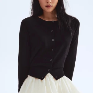 Svart kofta med knappar - En stilren svart kofta med rund hals och knäppning framtill. Koftan har långa ärmar och är tillverkad i ett mjukt stickat material som känns skönt mot huden. Perfekt att slänga över en topp för en enkel och clean look.