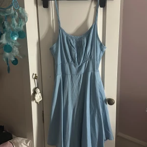 Ljusblå kort klänning med smala axelband - Supersöt ljusblå klänning med smala justerbara axelband och v-ringad byst med fina veckdetaljer. Klänningen har en lätt utställd kjol och dragkedja i ryggen. Perfekt för varma dagar och ger en fräsch vibe. Jätte söt klänning som inte kommer till användning längre för mig!! 💗 använt 1 gång innan ☺️