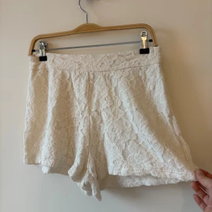 Vita spetsiga shorts - Vita shorts med snygg spets och blommigt mönster. De har en mellanhög midja och en diskret dragkedja bak för enkel påklädning. Materialet är mjukt och ger en lyxig känsla, perfekt för sommarens varma dagar. Passformen är normal och de är riktigt bekväma.