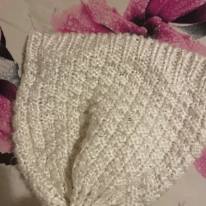 Vit stickad mössa med paljetter Kappahl - Snygg vit stickad mössa från Kappahl med glittriga paljetter och fluffig tofs på toppen. Mönstrad stickning och ribbad kant ger extra stilpoäng. Perfekt för dig som vill ha en mysig och trendig look under kalla dagar.