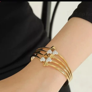 Snygg armband med hjärtan och strass i 14k guldpläterad  - Snyggt armband i 14k Guldpläterad med fyra smala band och dekorerade hjärtan i strass. Hjärtana är placerade i rad och ger en glittrig och romantisk vibe. Perfekt för dig som gillar detaljer och vill sticka ut med ett unikt smycke.