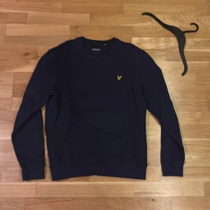 Mörkblå sweatshirt från Lyle & Scott - Mörkblå sweatshirt från Lyle & Scott med klassisk rund hals och ribbade muddar. Tröjan är i mjuk bomull och har en clean, normal passform som funkar till jeans eller chinos.