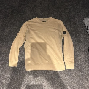 Beige sweatshirt från Lagency - Bara använt mycket få gånger. Pris kan diskuteras. Snygg beige sweatshirt från Lagency i storlek M. Tröjan har rund halsringning, långa ärmar och en svart patch med Lagency-logga på vänster ärm. Tillverkad i mjuk bomull för en skön känsla och stilren look.
