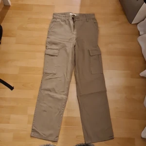 Beige cargopants med raka ben - Snygga cargopants i beige med raka ben och klassiska stora fickor på sidorna. Byxorna har midwaist och är tillverkade i slitstark bomull. Perfekta för dig som gillar en chill och praktisk stil med mycket förvaring.