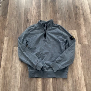 Grå half zip tröja Stone Island Junior - Snygg grå långärmad tröja från Stone Island Junior med klassisk badge på ärmen. Tröjan har half zip framtill och ribbade muddar vid ärmslut och nederkant. Perfekt för dig som gillar streetwear och vill ha något stilrent med cool detalj.