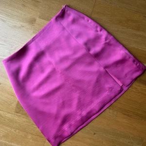 Kort satinkjol Neo Noir - Helt oanvänd kort satinkjol med liten slits framtill. Strl 34. Nypris 499.