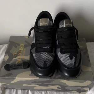 Valentino Rockrunner sneakers - Snygga Valentino Rockrunners i svart och grått med camouflagemönster. Skorna har mesh och mocka-paneler, svarta snören och platt sula med gummidetaljer. Storlek 44 kan passa 43. Fraktar samma dag. 