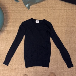 Mörkblå stickad tröja NN07 - Snygg mörkblå stickad tröja från NN07 med italienskt garn. Klassisk rund hals och långa ärmar, perfekt för dig som gillar stilrena och enkla plagg. Passformen är normal och materialet känns mjukt mot huden. Litet hål precis vid nacken