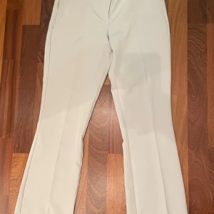 Vita kostymbyxor från Bik Bok strl 38 - Snygga vita kostymbyxor från Bik Bok i storlek 38. Byxorna har raka ben med lätt bootcut och pressveck framtill. De har bälteshällor och en diskret bakficka. Perfekta för en clean och fräsch look.