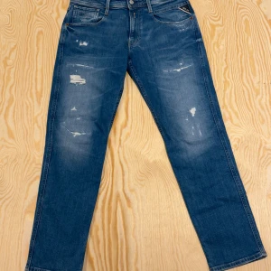 Replay Anbass slim jeans blå W31/L30 - Blå jeans från Replay, modell Anbass, med slim fit och klassisk femficksdesign. Jeansen har slitna detaljer och snygga kontrastsömmar och Replay-logga vid fickan.