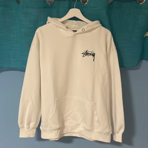 Vit Stussy Hoodie - Säljer denna snygga hoodien från Stussy eftersom den inte kommer till användning, den har vart använd ca 5 gånger och har mycket kvar att ge. Storleken är M, nypris är ca 1800kr. Hör av er vid frågor!