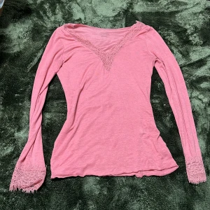 Rosa långärmad topp från Intimissimi - Supersöt rosa långärmad topp från Intimissimi med v-ringning och spetsdetaljer vid halsen och ärmsluten. Tillverkad i ultralätt material med kashmir för extra mjuk känsla. Perfekt för dig som gillar romantiska och feminina vibes.