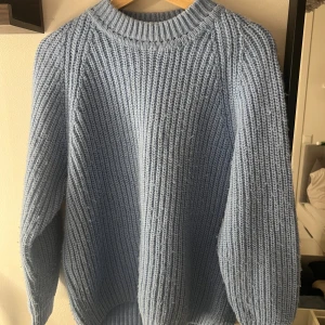 Ljusblå stickad tröja med rund hals - Säljer en mysig ljusblå stickad tröja med grov ribbad struktur och rund hals. Tröjan har långärmade ärmar och en relaxed passform som är perfekt för kyliga dagar. Enkel och stilren design som är lätt att matcha med jeans eller kjol.