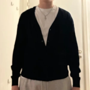 Mörkblå kofta från Uniqlo - Mörkblå kofta från Uniqlo i klassisk modell med v-ringning och knappar framtill. Långärmad och tillverkad i mjukt material som passar perfekt för lager-på-lager. Enkel och stilren design som funkar till många olika outfits.