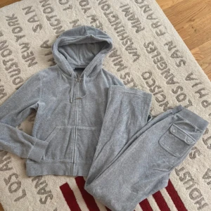 Grå mjukisbyxor Juicy Couture XS - Grå mjukisbyxor från Juicy Couture i storlek XS. Byxorna har bred resår i midjan med snörning, stora fickor fram och bak med lock och knappar. Mjukt bomullsmaterial som är superbekvämt och chill. Perfekt för att hänga hemma eller dra till gymmet.