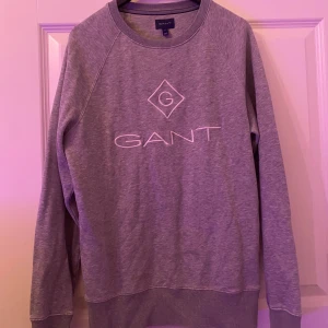 Grå sweatshirt från GANT - Säljer en stilren grå sweatshirt från GANT med broderad logga framtill. Tröjan har rund halsringning, långa ärmar och ribbade muddar. Perfekt för en chill och avslappnad look.
