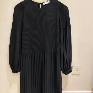  Ny supersnygg Svart plisserad klänning Cathrine Hammel - Supersnygg svart plisserad klänning från Cathrine Hammel i storlek XS. Klänningen har rund halsringning, långa puffärmar och ett elegant fall. Materialet är mjukt och har en lyxig känsla, perfekt för dig som gillar stilrena och moderna plagg.