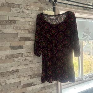 Mönstrad kortklänning från me&i - Säljer en färgstark kortklänning från me&i i storlek L. Klänningen har ett unikt cirkelmönster i rosa, gul och grått på svart botten, med rund hals och trekvartsärmar. Mjuk och skön bomullskvalitet som är perfekt för dig som gillar att sticka ut.