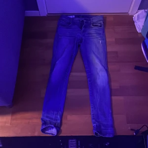 Replay blå slim jeans med dragkedja - Snygga blå jeans från Replay i slim fit-modell med klassisk femficksdesign och dragkedja. Jeansen har lätt slitna detaljer och är tillverkade i mjukt bomullsmaterial med lite stretch för extra komfort. Passar dig som gillar en modern och smal siluett.