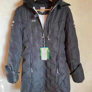 Marinblå ridkappa från Uhip, storlek 36 - Snygg och funktionell rid parkas från Uhip i marinblå .kappan har huva, långa ärmar, flera dragkedjor och smarta detaljer. Perfekt för kalla dagar med sin quiltade design och längre modell. Märke broderat på bröstet och reflexdetaljer på ärmarna. Helt ny och icke använd. Nypris 2995:- 