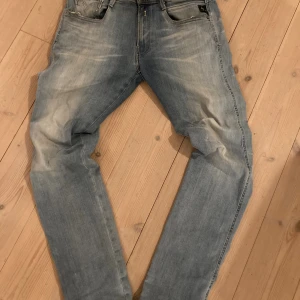 Replay Hyperflex ljusblå jeans - Snygga ljusblå Replay Hyperflex jeans med slitna detaljer och klassisk femficksdesign. Jeansen har en slim passform och är tillverkade i stretchigt jeansmaterial för extra komfort. Perfekt för dig som gillar en avslappnad men trendig look.