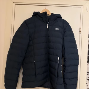 Mörkblå pufferjacka från Icebound - Säljer en mörkblå pufferjacka från Icebound med huva och dragkedja framtill. Jackan har quiltad design, två sidofickor med dragkedja och logga på bröstet. Perfekt för kalla dagar och har en clean, sportig look.nypris 1200kr, använd 2månader