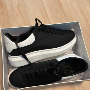 Alexander McQueen svarta sneakers - Säljer ett par svarta Alexander McQueen sneakers med vit häl och tjock vit plattformssula. Skorna har svart snörning och är tillverkade i skinn. Klassisk och clean design med logga på hälen och sula.