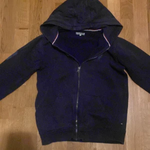 Mörkblå hoodie från USPA/Polo med dragkedja - Snygg mörkblå hoodie från USPA med broderad logga på bröstet och praktisk huva. Tröjan har hel dragkedja framtill, två fickor och ribbade muddar. Perfekt för chill dagar och har en klassisk look med sportig touch.