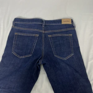 Diesel Bashila slim-skinny jeans blå - Snygga blå jeans från Diesel, modell Bashila med slim-skinny passform och regular midja. Klassisk femficksdesign, slitna detaljer framtill och kontrastsömmar. Tillverkade i Italien i slitstarkt denimtyg. Perfekt för dig som gillar en smal siluett.