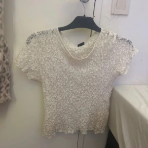 Vit spetsblus från Gina Tricot - Säljer en söt vit blus från Gina Tricot i storlek M. Blusen har korta ärmar och är helt täckt av spets med blommigt mönster. Den har rund halsringning och är lätt croppad i modellen. Perfekt för dig som gillar romantiska detaljer och vill ha en feminin look. Ny skick, andvänd 1-2 ggr, skriv för fler frågor ❤️