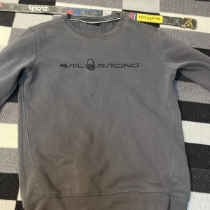 Mörkgrå Sail Racing sweatshirt - Snygg mörkgrå sweatshirt från Sail Racing med stilren logga broderad på bröstet. Tröjan har rund hals, långa ärmar och en clean look utan extra detaljer. Perfekt för dig som gillar sportiga och minimalistiska plagg.