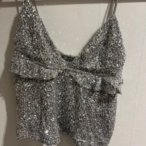 Glittrig silver tubtopp från Subdued - Säljer en glittrig tubtopp från Subdued i silver med paljetter över hela toppen. Perfekt för att sticka ut och ge extra bling till din outfit.