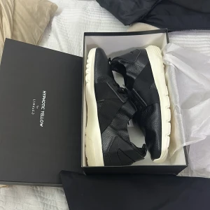 Svarta sneakers Hypnotic Yellow x Lynk&Co - Snygga svarta sneakers från Hypnotic Yellow för Lynk&Co med vit, chunky sula. Skorna har en modern design med mix av skinn och textil, snörning och breda elastiska band över foten. Perfekta för dig som gillar stilrena och unika detaljer.