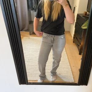 Grå straight fit Jeans - Säljer ett par grå jeans med klassisk straight fit och normal passform. Jeansen har fem fickor, silverfärgade knappar och dragkedja. Materialet är slitstarkt denim och färgen är ljusgrå med diskret tvättad look. Perfekt för dig som gillar tidlös stil.