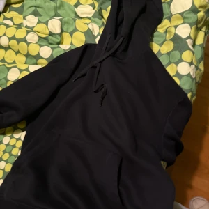 Svart hoodie med huva och ficka - Svart hoodie med stor magficka och snörning vid huvan. Perfekt för dig som gillar en enkel och clean look. Tröjan har lång ärm och är gjord i mjukt material som känns skönt mot huden.