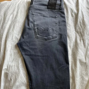 Grå jeans från Replay straight fit - Säljer ett par grå jeans från Replay med klassisk femficksdesign och diskret broderad bakficka. Jeansen har rak passform och är tillverkade i mjukt denimtyg som sitter skönt hela dagen. Perfekta för dig som gillar en clean och stilren look.