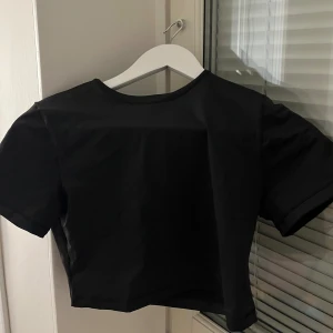 Svart croppad bad topp från Skims - Svart croppad topp från Skims med rund hals och korta ärmar. Tillverkad av återvunnen nylon och spandex för en mjuk och stretchig känsla. Använd istället för bikinitopp. Oanvänd men testad sen tvättad