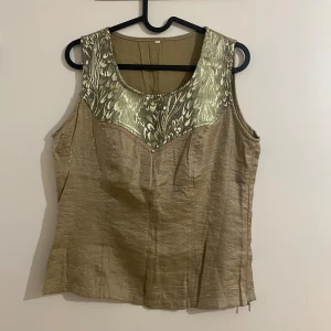 Oliv färgad topp - Säljer en snygg olivfärgad linnetopp med metallic finish och bred, mönstrad panel. Toppen är ärmlös med rund halsringning och har en lätt skimrande struktur i tyget. Perfekt för dig som vill sticka ut lite extra!