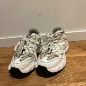 Chunky vita sneakers Aim'n strl 36 - Chunky vita sneakers från Aim'n i storlek 36. Skorna har en cool, sportig design med svarta och grå detaljer, snörning och tjock sula. Ovandelen är i syntetmaterial och mesh för extra andningsförmåga. Perfekta för dig som gillar streetstyle och bekväma skor.
