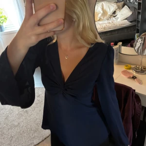 Mörkblå blus med v-ringning och twist - Säljer en mörkblå blus med långärmade, lätt utsvängda ärmar och snygg v-ringning med twistad detalj framtill. Blusen har en feminin passform och är perfekt för dig som gillar stilrena plagg med det lilla extra.